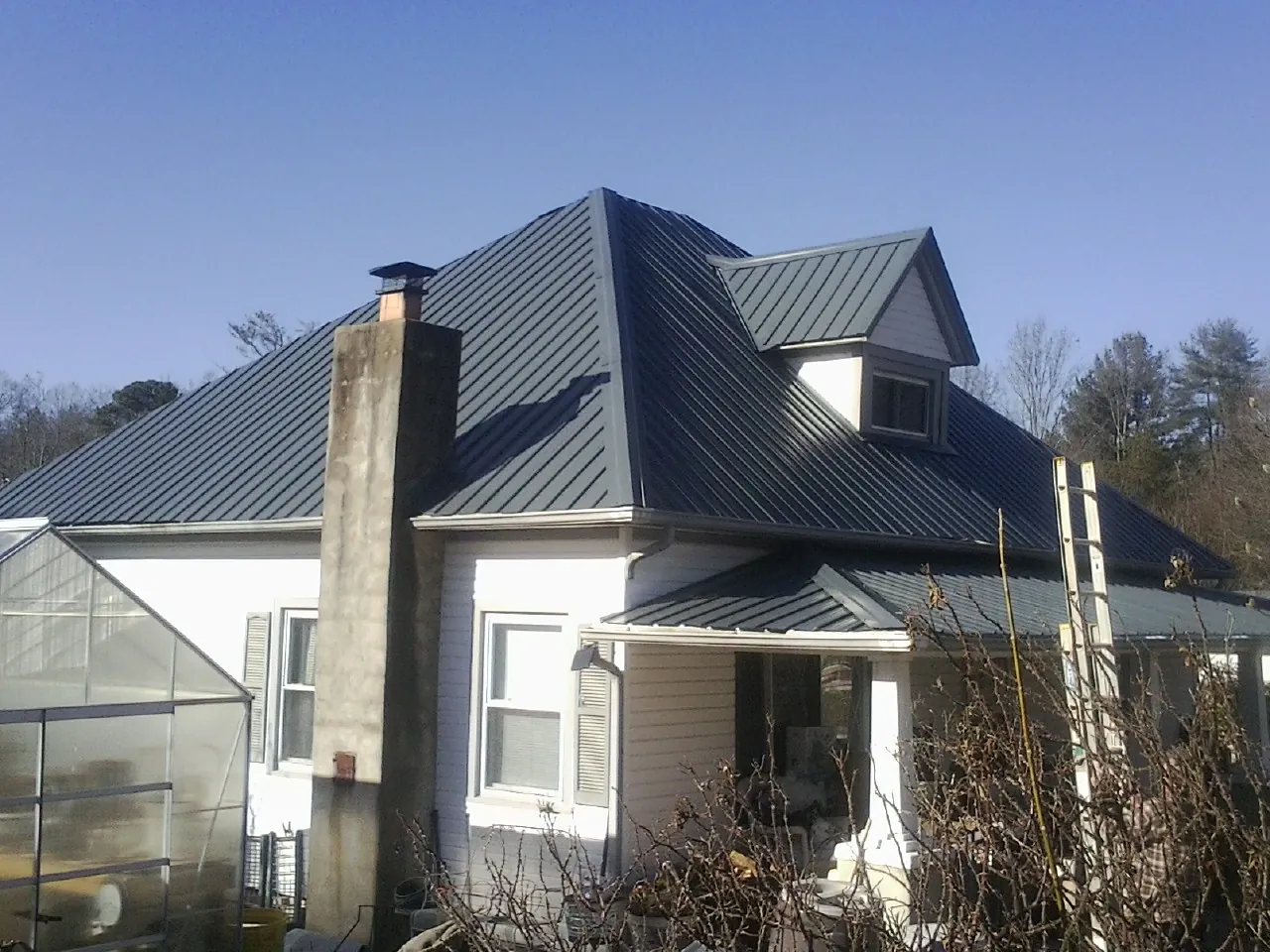 Dark blue standing seam metal roof on a white farmhouse with dormer — Slate & Tile Roof Repair by Roofing Brothers in Harbert