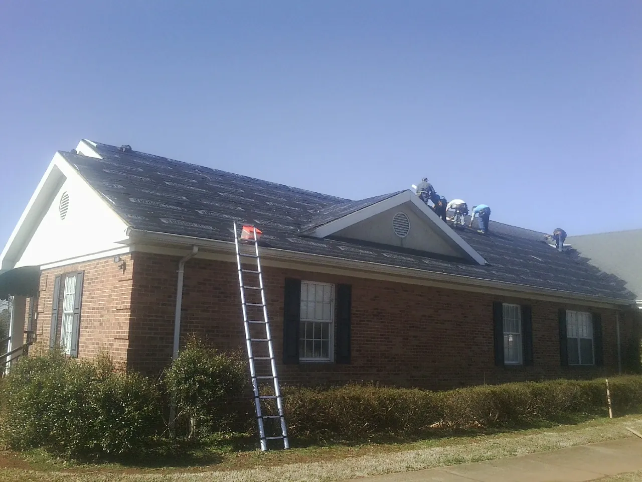 Crew tearing shingles off a brick ranch roof with a ladder set — Metal Roof Repair work by our crew in Harbert