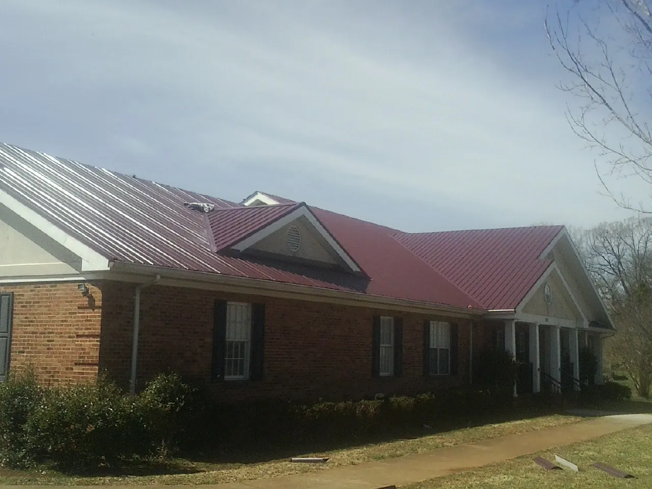 Red metal roof with gabled entries on a long brick building, from a Hail Damage Roof Repair job in Harbert