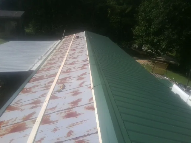 Old rusted panels beside newly installed green metal roofing — Wind Damage Roof Repair by Roofing Brothers in Harbert