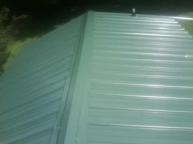 New green metal panels meeting at the ridge of a roof — Flat Roof Repair work by our crew in Harbert