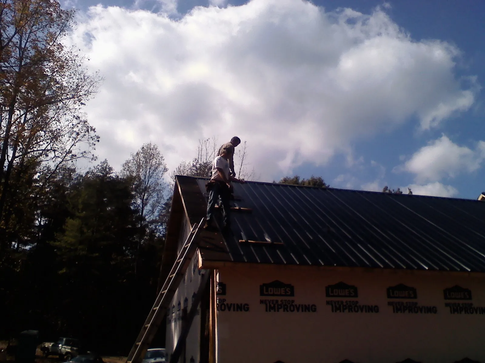 Roofer fastening dark metal panels high against a cloudy sky, from a Roof Inspection job in Harbert